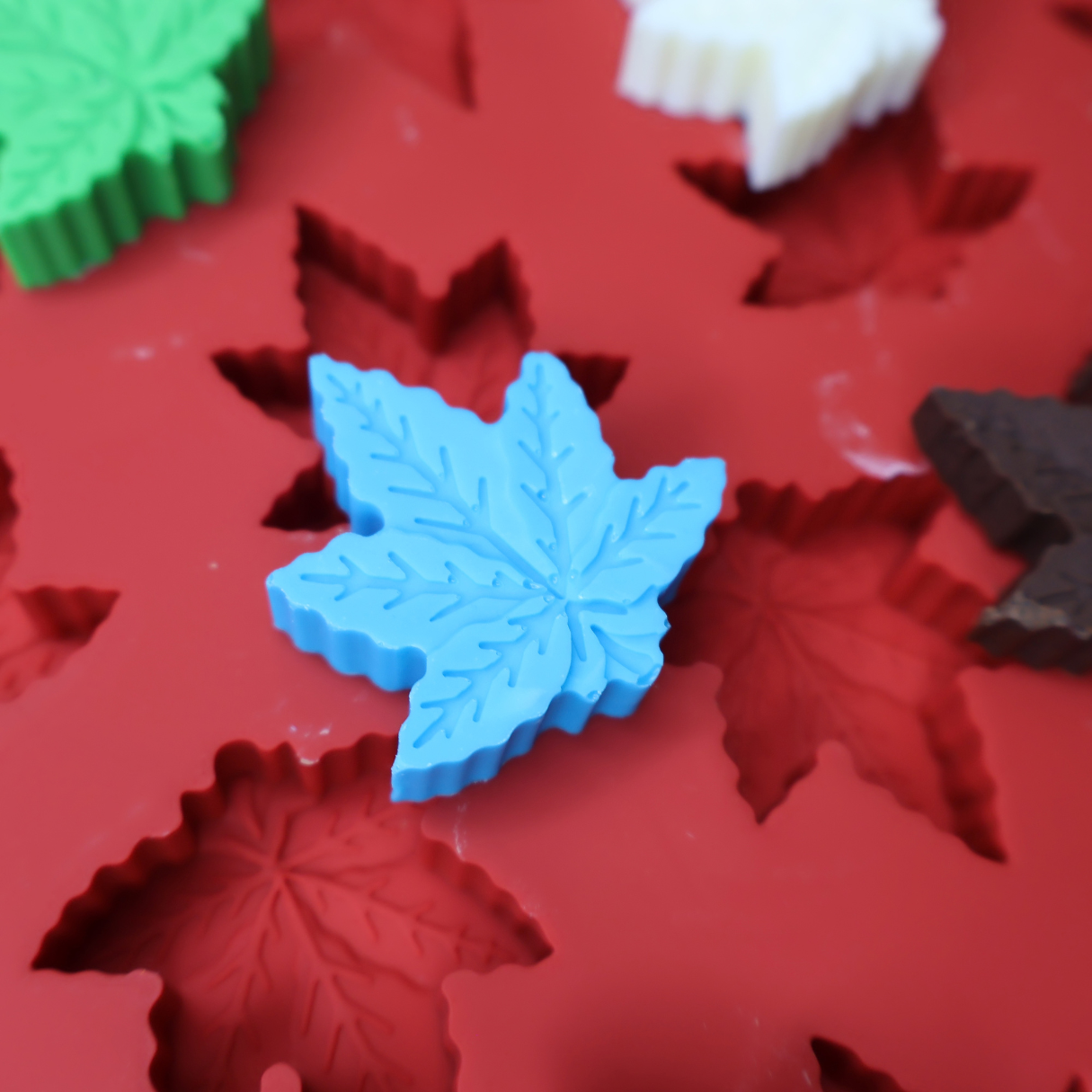 A blue canna leaf-shaped item resting on a red silicone mold tray with leaf-shaped cavities, with other leaf-shaped items partially visible in the background.
